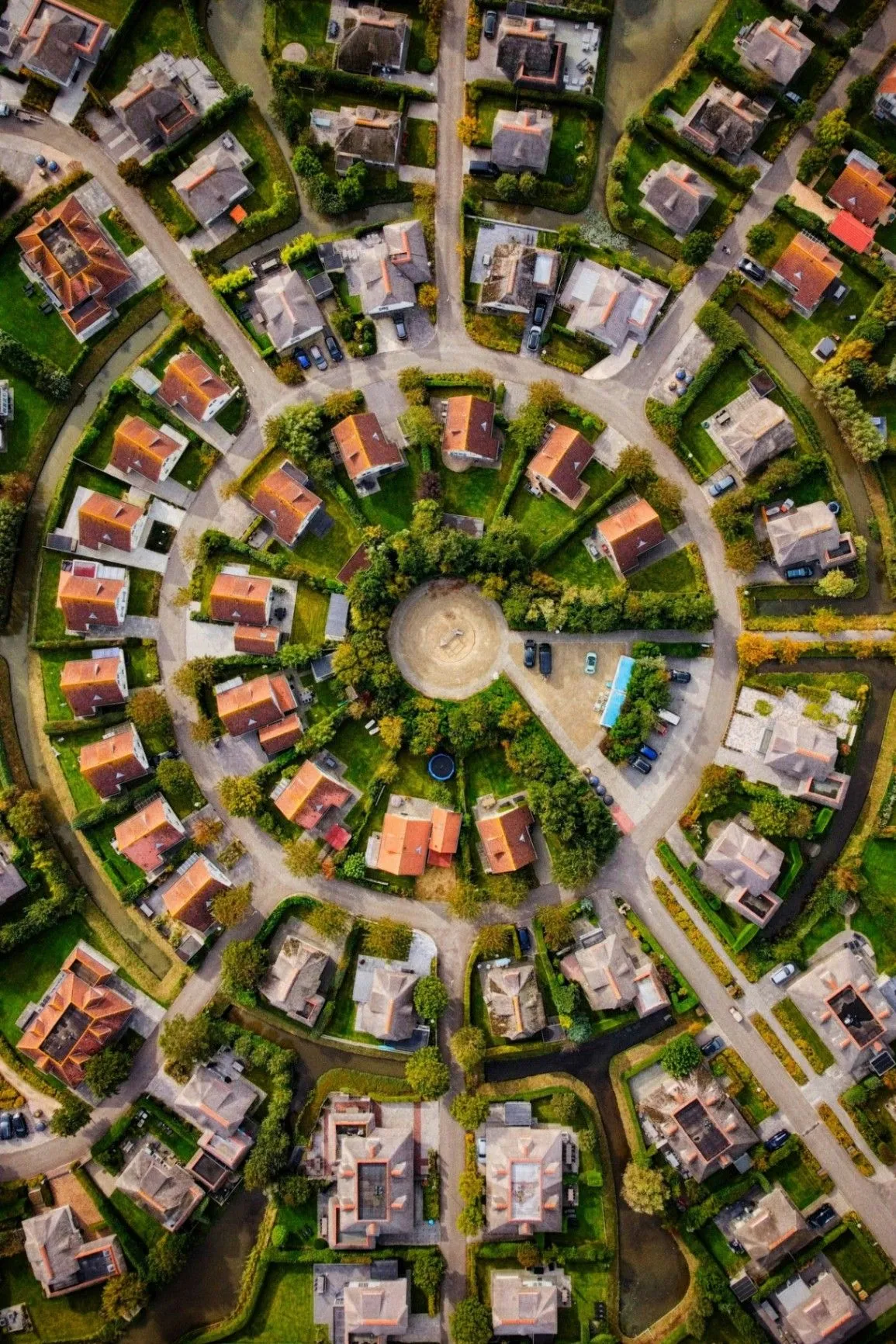 Aerial view of a residential neighborhood with curved streets, red-roofed houses, green trees, and canals
